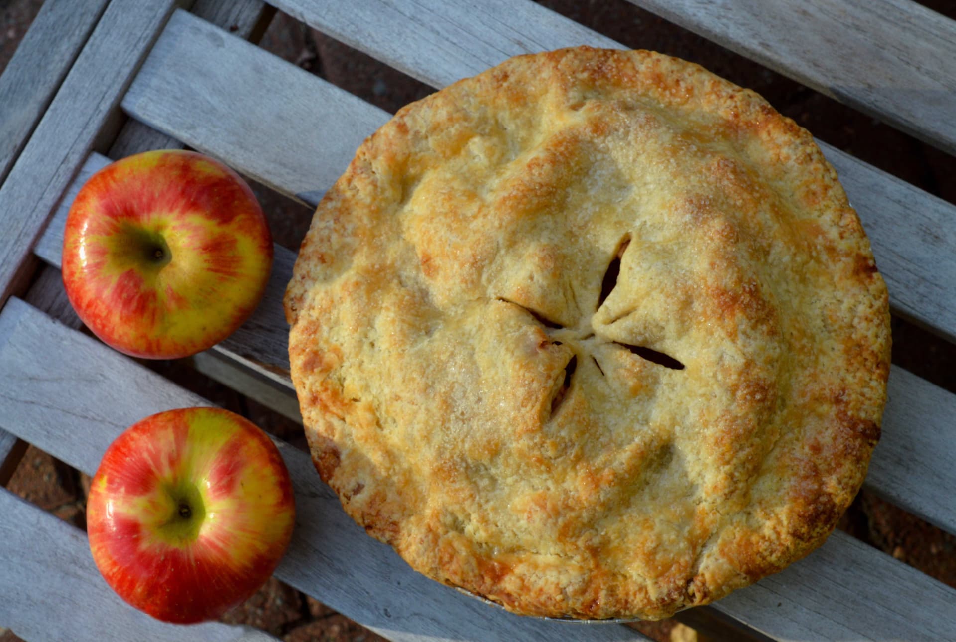 Vegan apple pie on wooden bench with two apples
