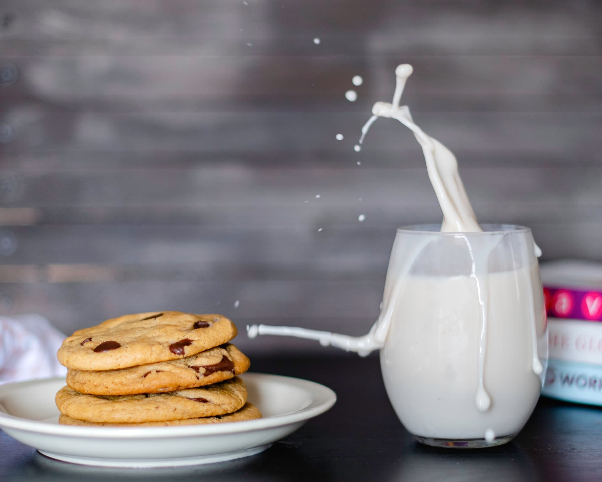 Cookies on white plate next to glass of milk with splash