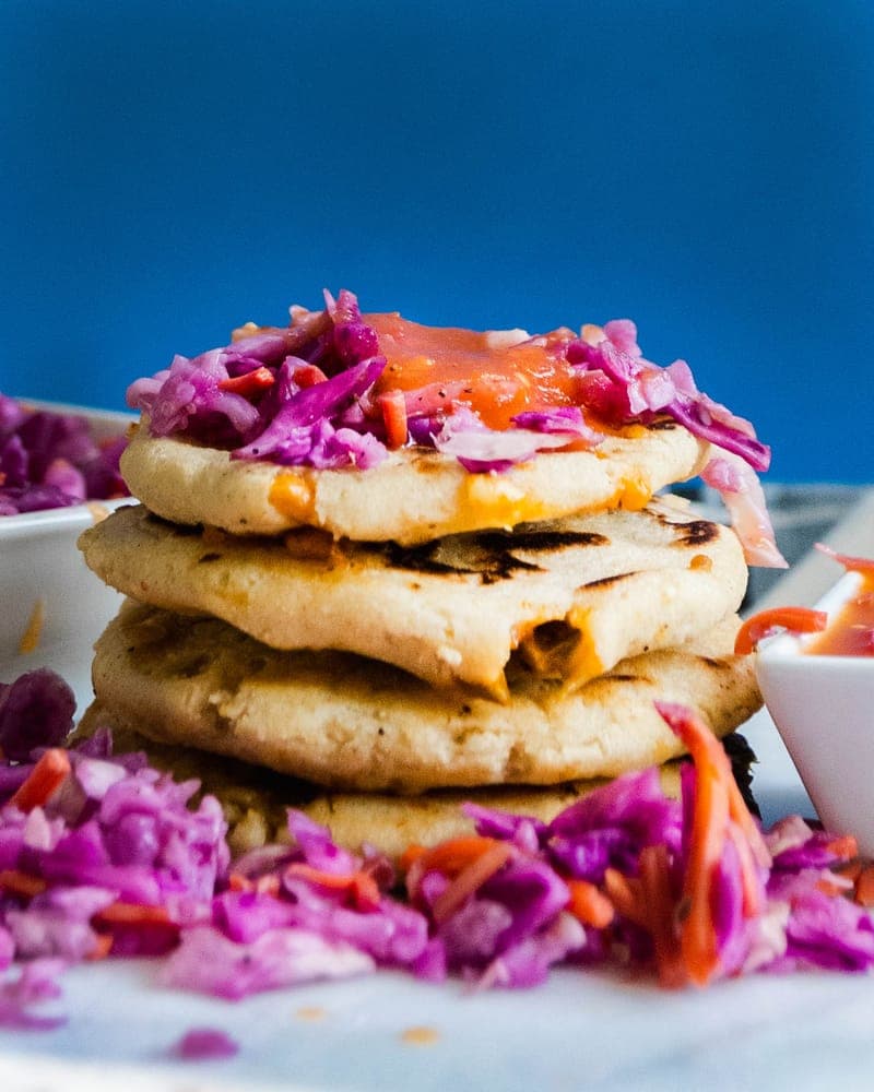 Stack of vegan pupusas topped with purple cabbage slaw and sauce